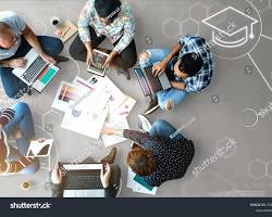 Vue de dessus d'un groupe de personnes assises autour d'une table en bois, travaillant ensemble sur des ordinateurs portables et prenant des notes.