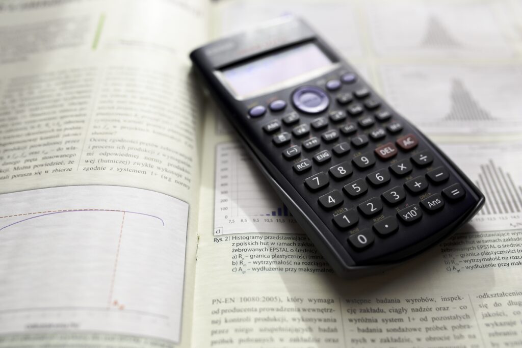 Une calculatrice scientifique noire posée sur la page ouverte d'un manuel scolaire affichant des graphiques de courbes et d'histogrammes.